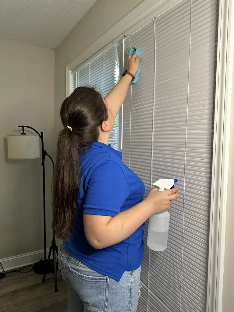 Bozman Cleaning team member wiping residential window blinds
