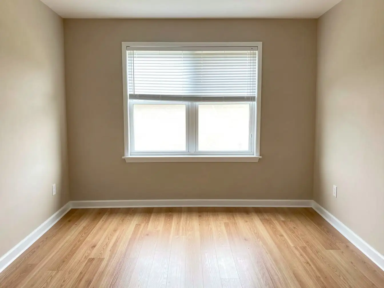 Empty bedroom with clean laminate floor, white baseboards and a window with raised blinds